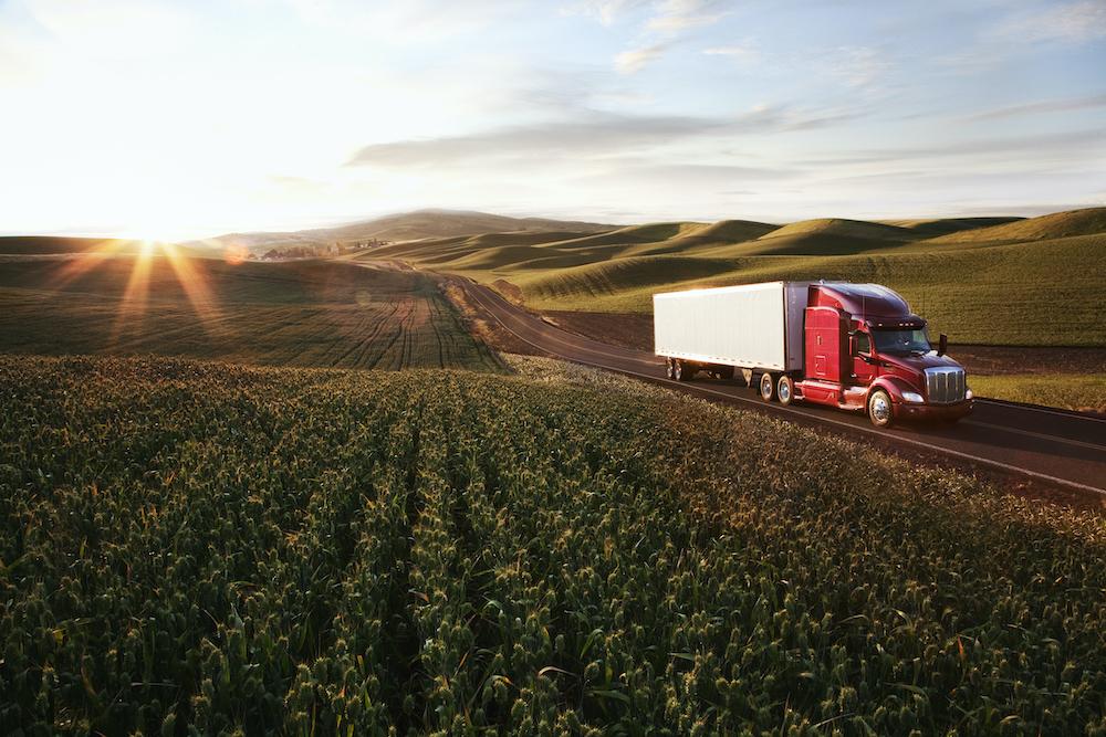 Semi truck rolling down a highway through fields at sunset