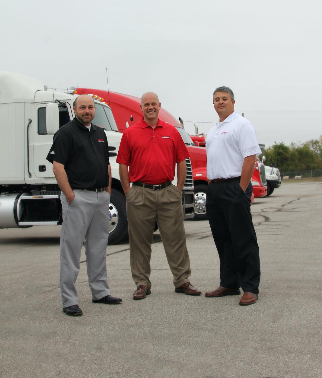 Image of 3 arrow reps standing in front of parked semi trucks.